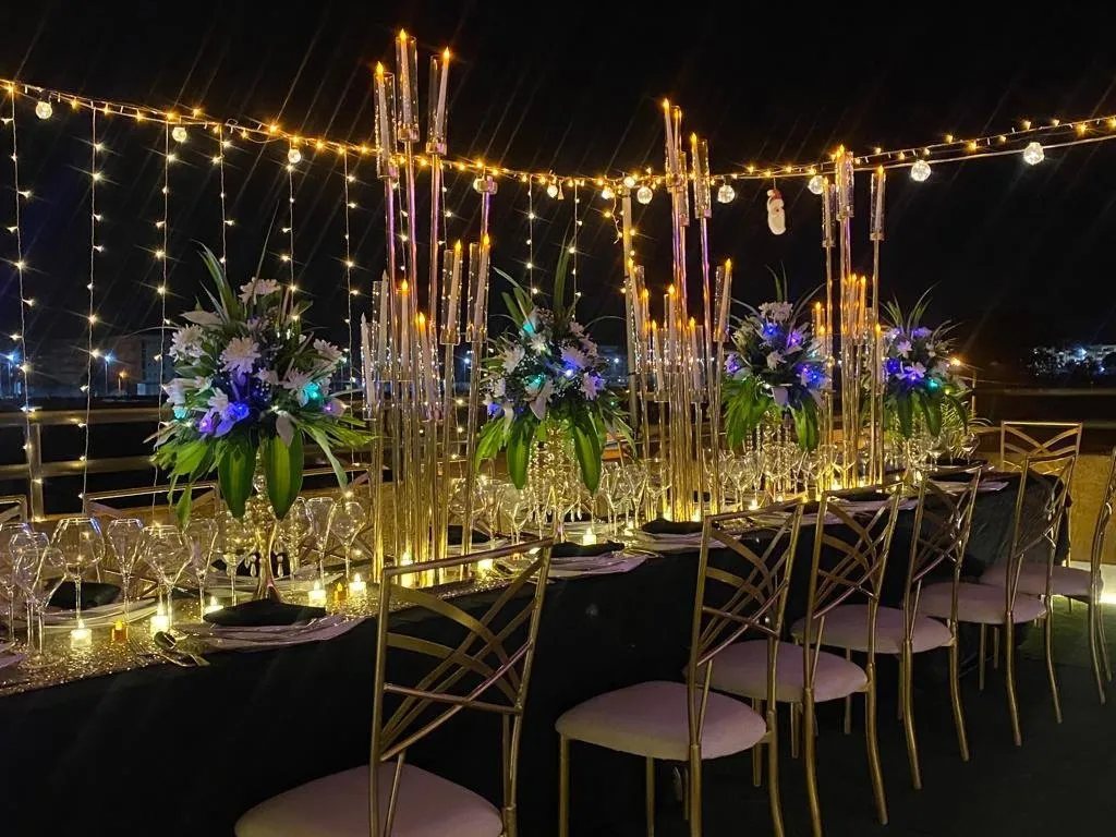 Longue table dressée en terrasse sous des guirlandes lumineuses, à la tombée du jour