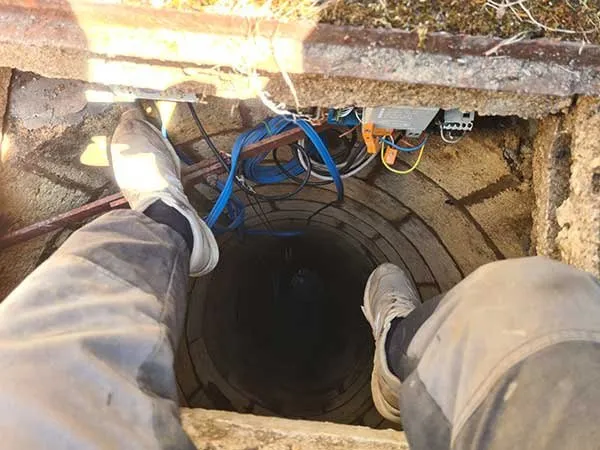 Descente dans un ouvrage de captage : cuvelage maçonné, colonne et raccordements électriques en tête